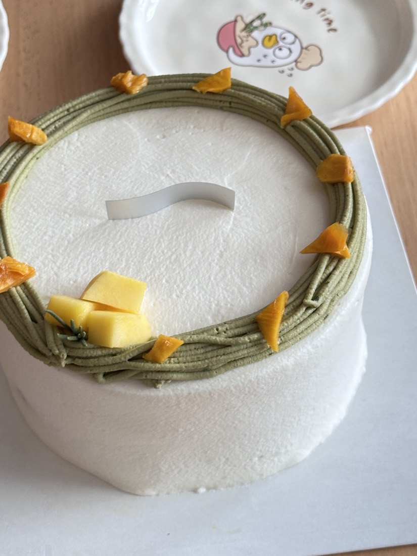 White cream cake ringed with piped matcha cream and fresh mango pieces