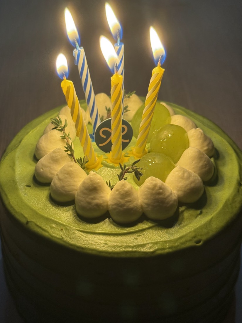 Matcha cake with lit birthday candles and a gold Mille monogram disc