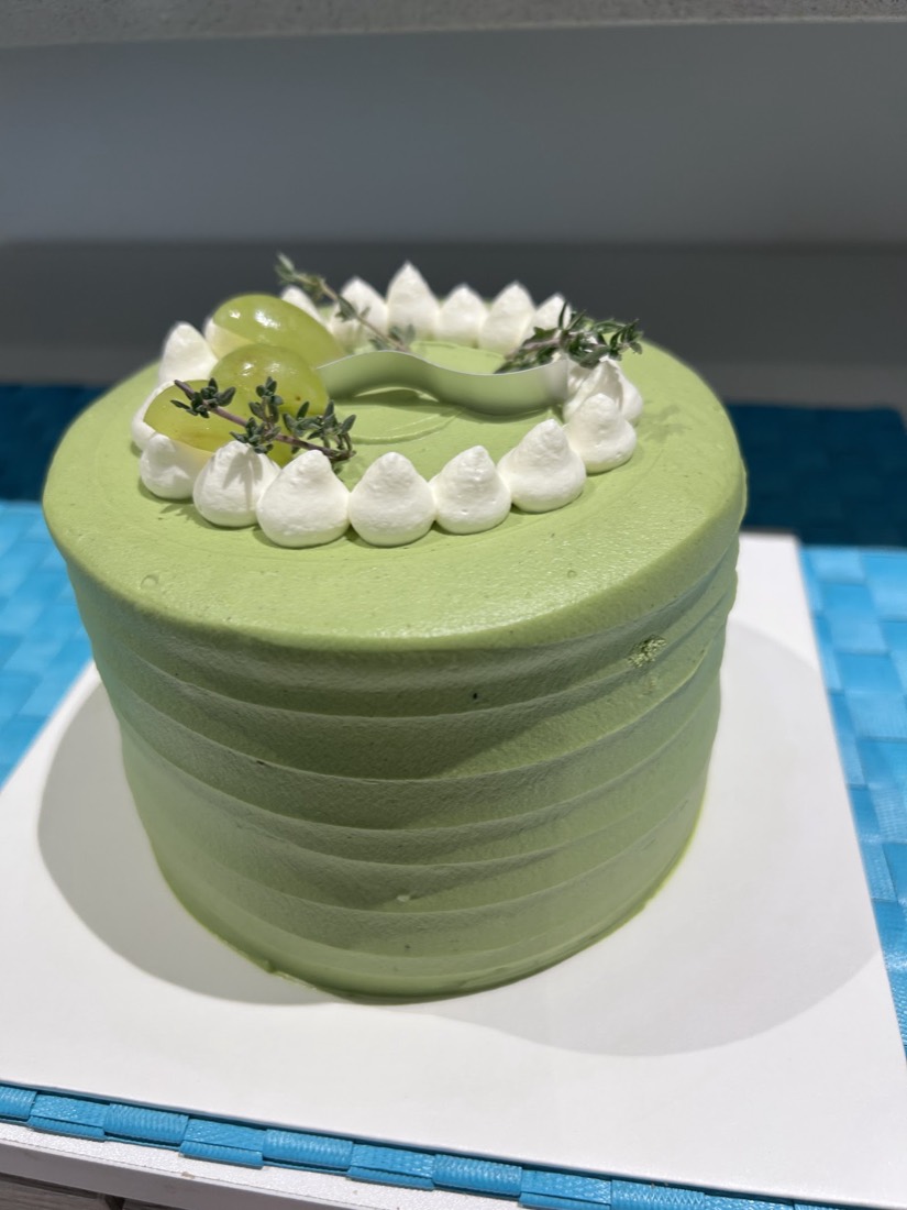 Matcha cream cake topped with piped cream, green grapes and thyme