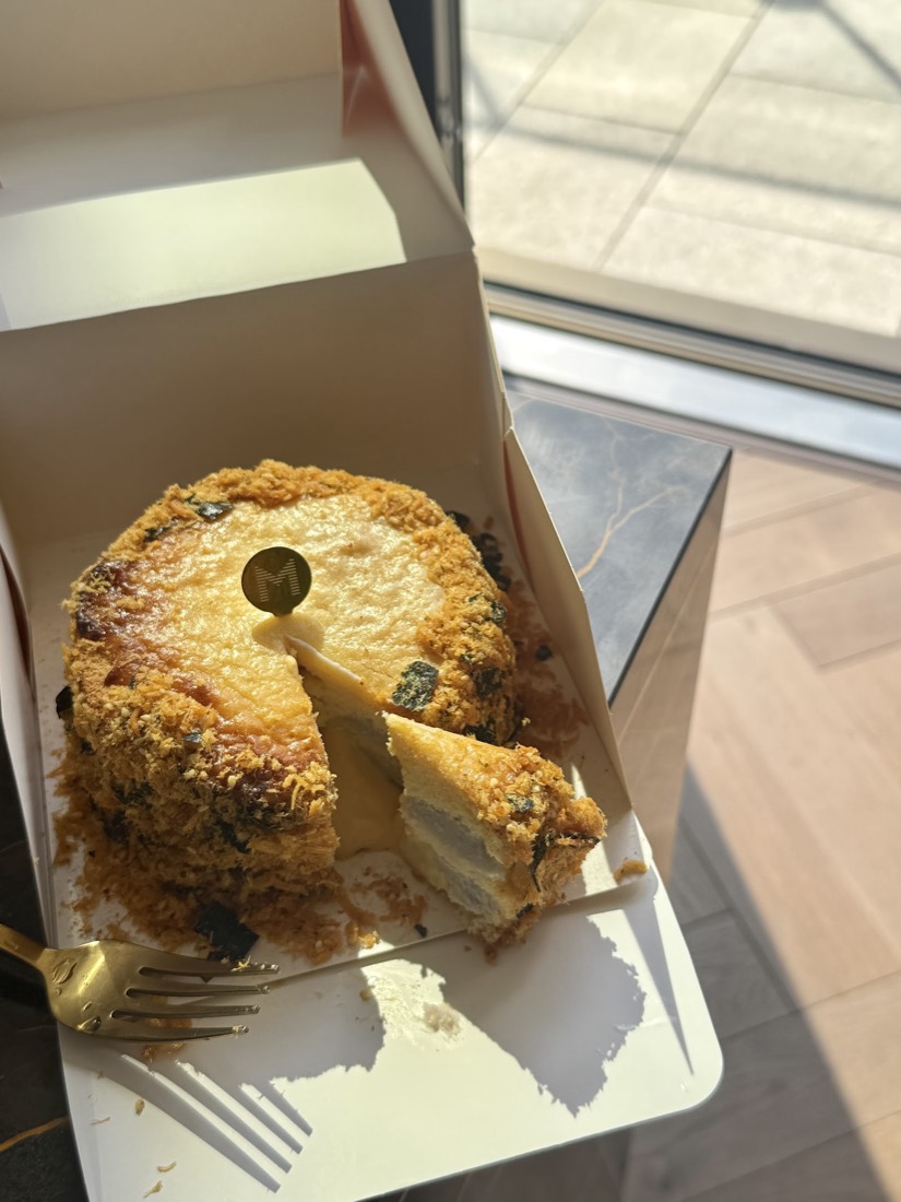 A salted-egg-yolk sponge cake crusted with chicken floss and seaweed, cut to show its cream layers, topped with a gold Mille disc
