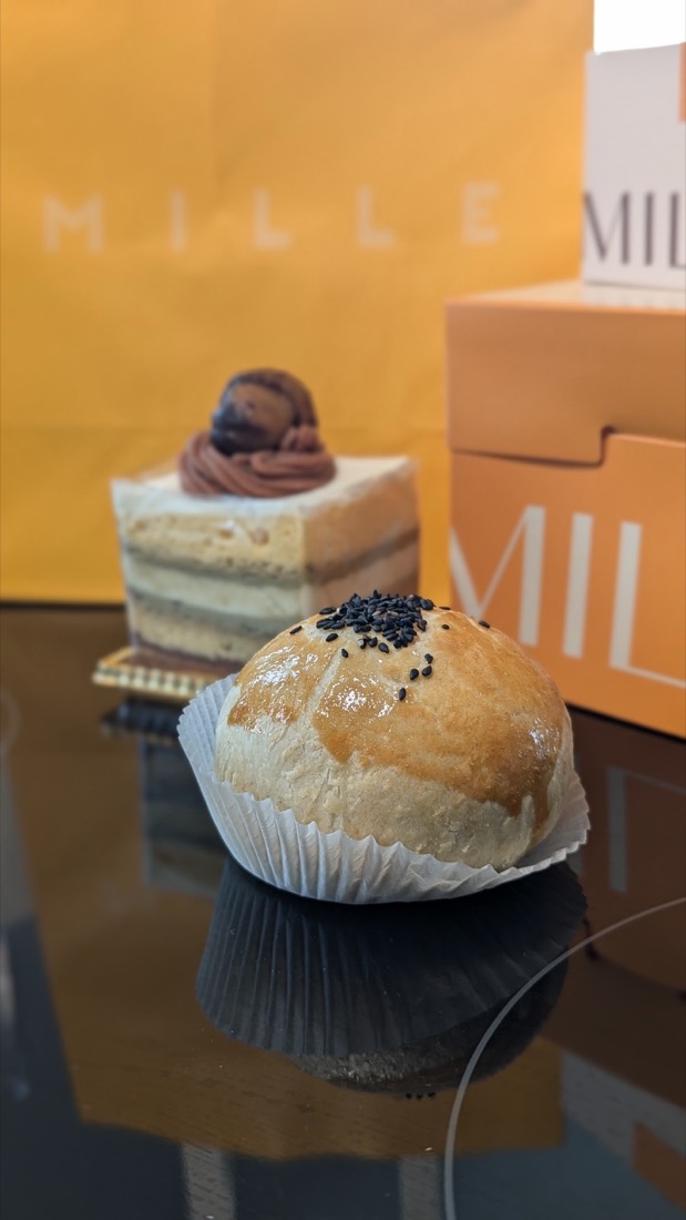 Mille-branded boxes and bag in amber and orange, with a black sesame bun and a slice of layered cake